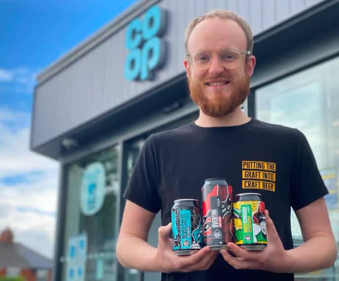 Jack from Docks Beers holding core range cans at a Co-Op store