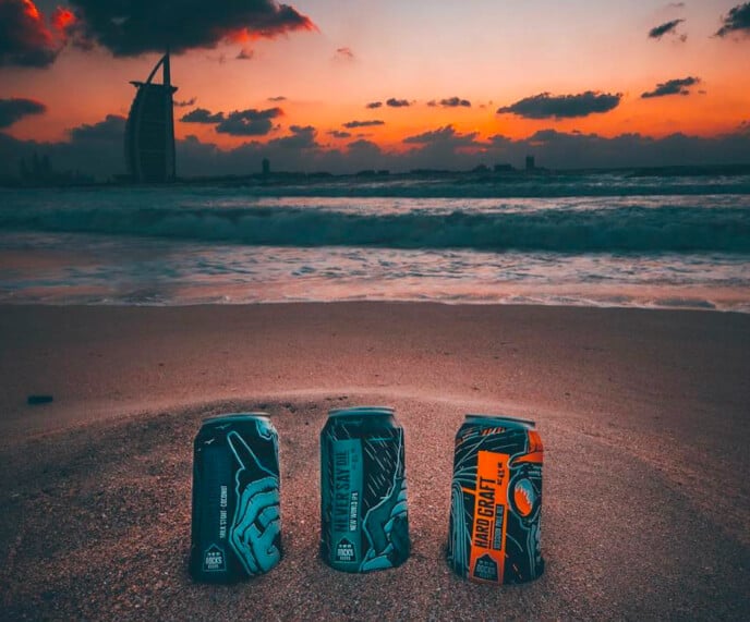 Docks Beers core range cans on a beach at sunset in Dubai